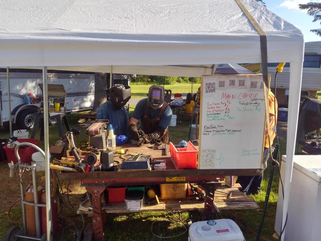 Mancamp 2018 at Porcfest — campers and mentors working under a tent with a price-list whiteboard